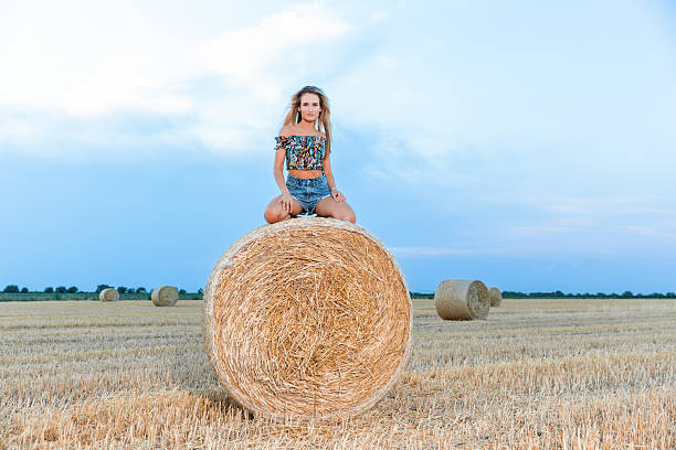 istock Young woman sitting on a round haystack in a mowed field 2231309035