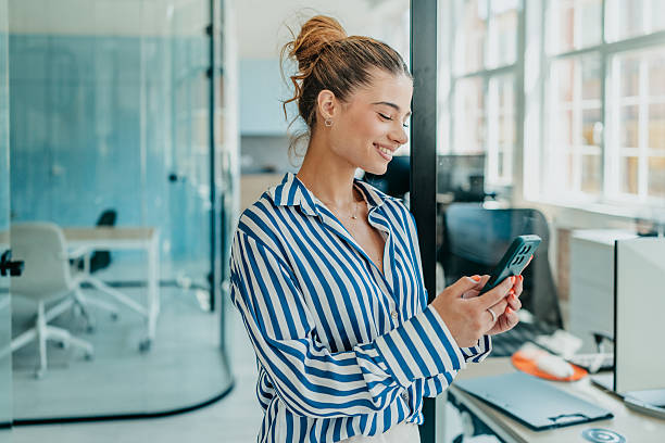 istock Young woman enjoying her time in a bright office while using her smartphone and smiling cheerfully 2231311765