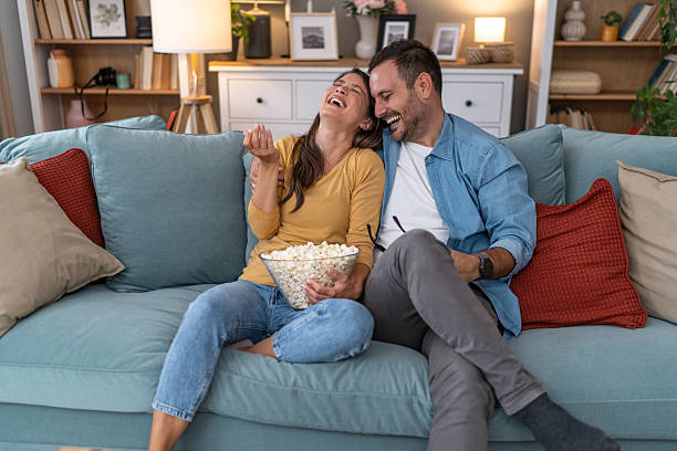 istock Couple laughing and eating popcorn while watching tv at home 2231314436
