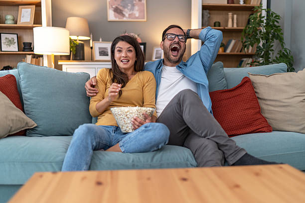 istock Excited couple watching tv and eating popcorn on sofa 2231314460