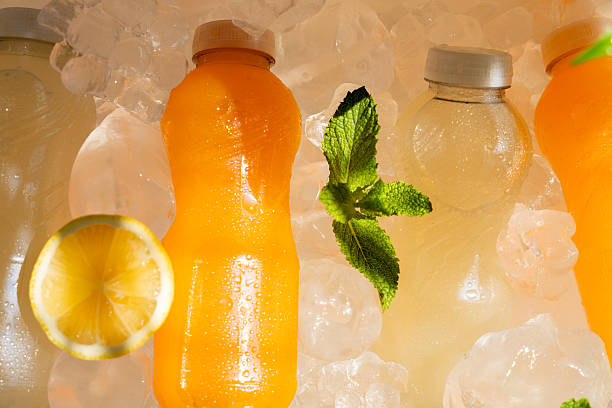 Plastic bottles of orange and lemon juice cooling on ice with lemon slice and fresh mint leaves