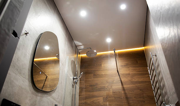 Spacious and elegant modern bathroom designed for master bedrooms, upscale villas, apartments, or hotels. The space features two black stone oval vessel sinks with sleek wall-mounted black faucets. Behind each sink, large round mirrors are mounted on a stunning accent wall made of vertical wood slats, adding warmth and texture to the minimalist aesthetic. The floor and walls are covered with large-format natural stone tiles in neutral tones, creating a seamless, luxurious look. Discreet spotlights in neutral LED color and a hidden blue LED strip provide ambient lighting, enhancing the calming and spa-like atmosphere. Perfect for showcasing premium bathroom design, contemporary fixtures, and architectural interiors.