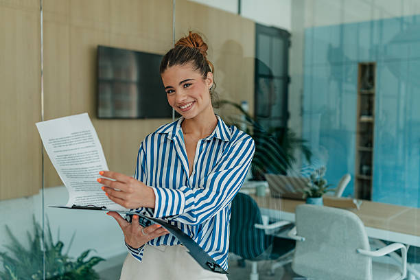 istock Young woman smiling while holding documents in a bright, modern office during a cheerful day 2231316812
