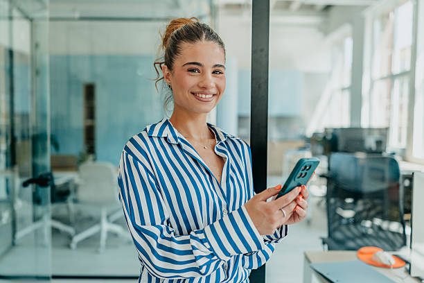 istock Young woman smiling while using her smartphone in a bright and modern office 2231317024