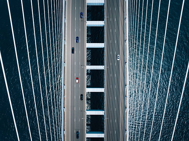 An overhead perspective of vehicles crossing on a modern cable-stayed bridge over calm blue waters, showcasing symmetry, design, and functionality.