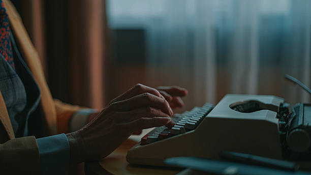 Hands of a man in a suit operating a vintage typewriterin a dimly lit room with cinematic light. Location: indoor setting.