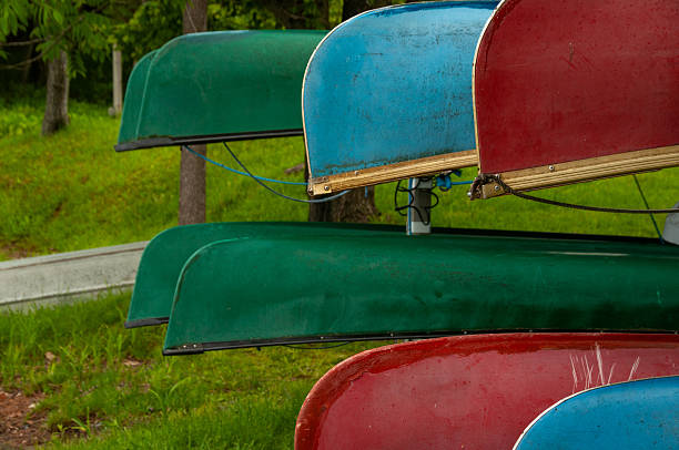 A close-up of colorful canoes hanging upside down on a rack outside over grass.
