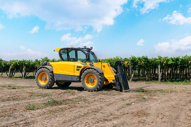 Forklift loader of yellow color in a field on a vineyard background.