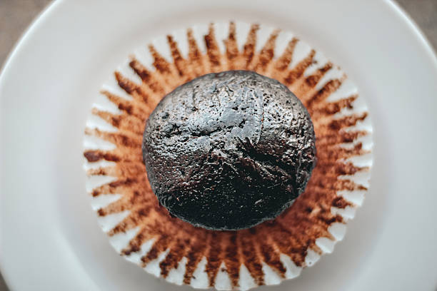 Looking down on a rich dark chocolate muffin on a white crinkly paper liner.