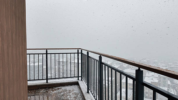 Heavy snowfall obscures the view from a balcony above a city blanketed in white.