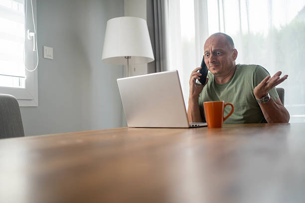 istock Confused man looking at laptop while talking on smartphone at home frustrated with poor customer support service 2231333926