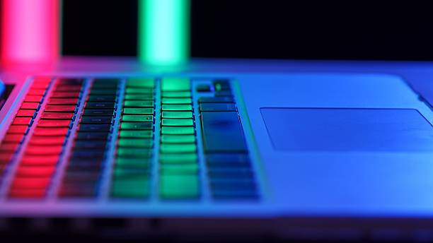 A laptop keyboard under vibrant neon lighting, highlighting colorful keys in a dark environment.