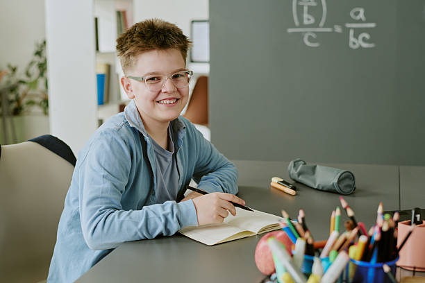 istock Portrait of Caucasian Boy Smiling While Writing in Notebook at Classroom Desk 2231338056