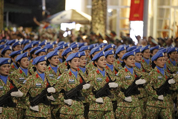 Military training: armed female  soldier in camouflage gear taking a break armed with with rifle against the outdoor wall, during practising military discipline and teamwork.