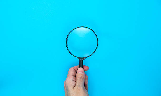 istock Man hand holding a magnifying glass on blue background 2231342980