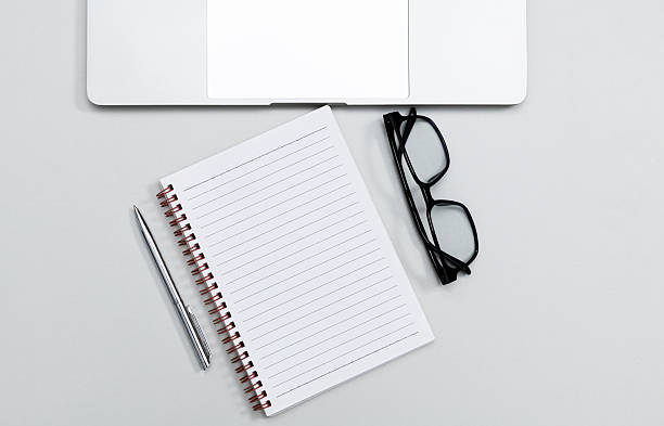 Office desk with blank notebook page, laptop computer, pen and eyeglasses