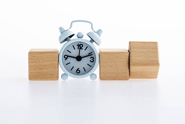 Alarm clock and turned wooden block on white background
