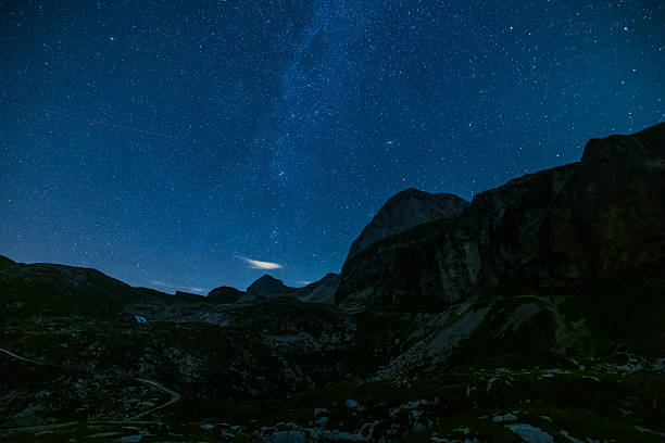 Mangart Mountain towers over Mangart Saddle with a clear starry sky above. The Julian Alps alpine landscape is illuminated under the night sky filled with countless stars.
