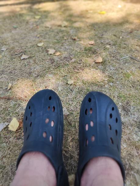 istock Man wearing black clogs standing on dry grass in the park during summer 2231345884