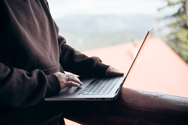 istock Young man with laptop on balcony in hotel with mountain view. 2231354361
