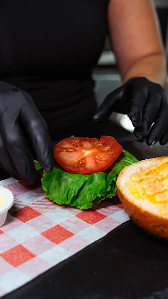 istock Cook adding tomato slice to lettuce on hamburger bun in restaurant kitchen 2231355024