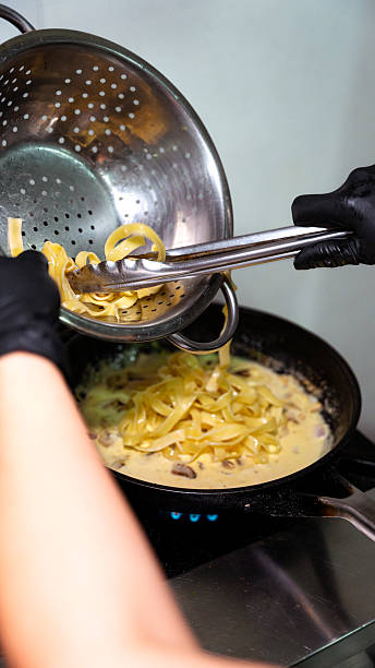 istock Chef combining pasta and creamy sauce in a pan 2231356058