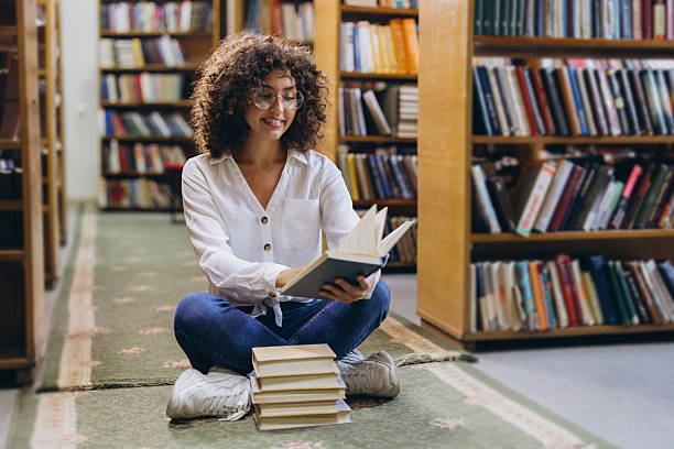 istock Young student reading a book sitting on the floor in the library 2231359651