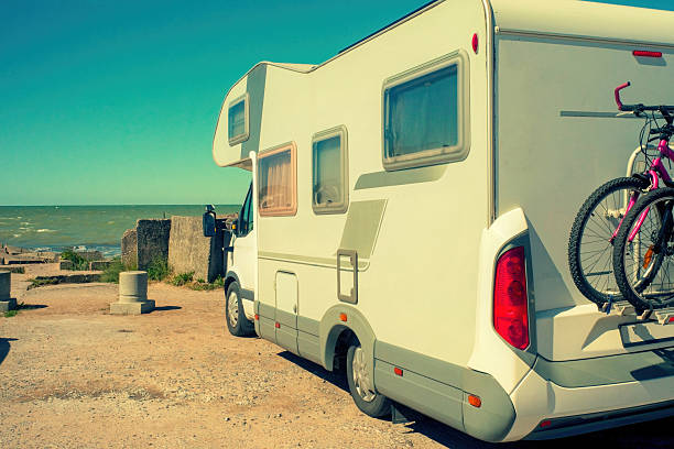 A camper van with a bicycle mounted on the back is parked near the sea on a sunny day. Concept of travel, freedom and summer vacation.