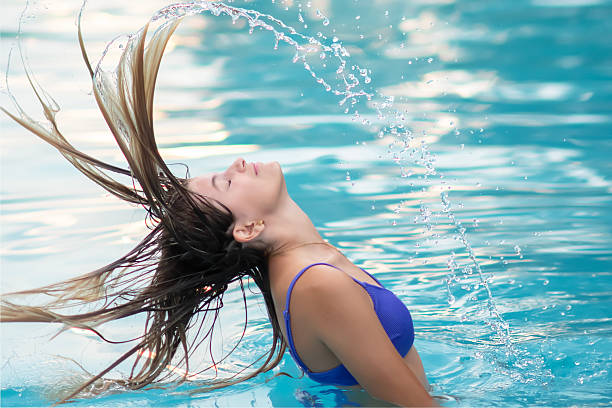 Young woman in swimming pool flips wet hair back dramatically, creating splashes of water and beautiful lines of water movement. Water games. Summer vacation