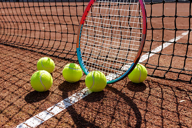 Closeup racket and bright balls on clay line under a net shadow perfect for club lessons coaching ads and tournament promotions.