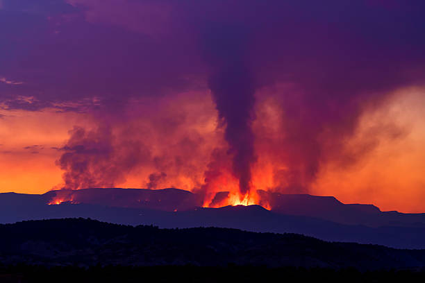 Derby Forest Fire Wildfire Flat Tops Colorado - Large plumes of smoke and visible flames and fire from burning forest in the mountains of the Flat Tops Wilderness with warm sunset glow colors as a backdrop. Large destructive forest fire and giant clouds of smoke and haze captured at twilight dusk blue hour.