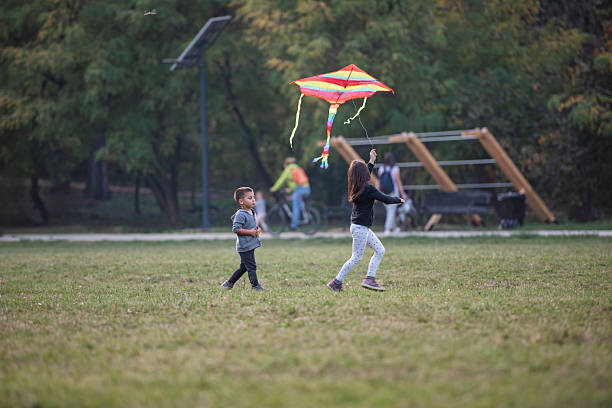 Two joyful children running and playing with a vibrant kite in a lush green park, enjoying a sunny autumn day filled with laughter