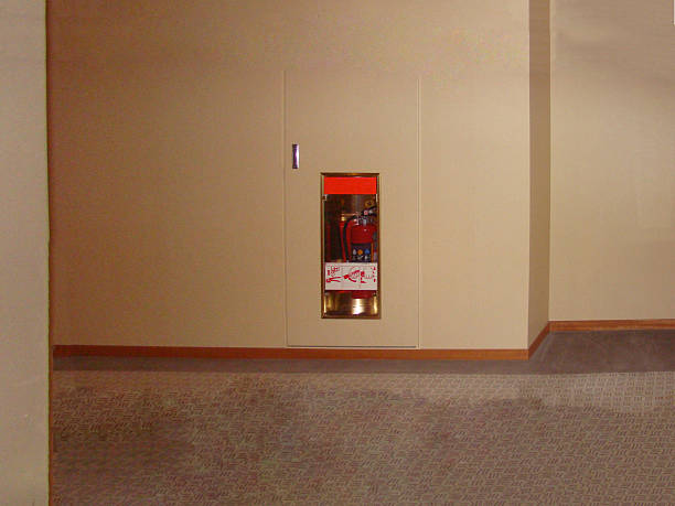 A wall-mounted fire extinguisher in a recessed cabinet along a hallway with carpeted flooring. The area is clean and orderly, illuminated by soft lighting, highlighting the safety measures in the space. The extinguisher is placed discreetly for emergency accessibility, contrasting with the neutral tones of the surroundings, emphasizing preparedness.