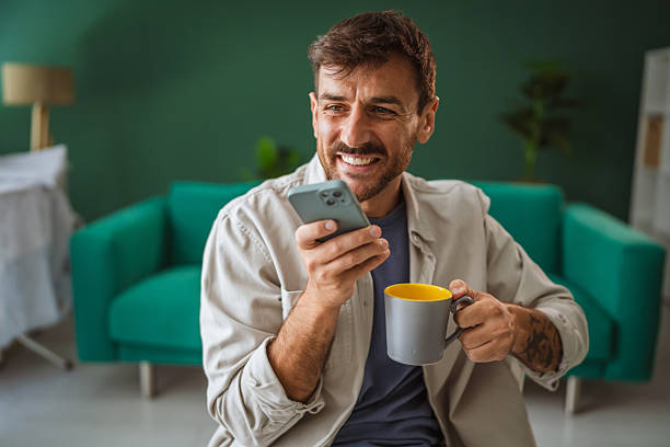 istock Smiling man using smart phone and drinking coffee at home 2231376533