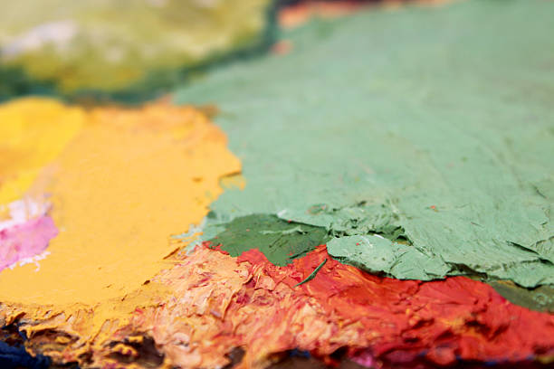 Palette knives resting on an artist's palette with oil paints and a blurred painting in the background
