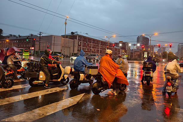 Beijing, China - Aug21, 2025: People on bikes waiting for traffic lights in rain at night.