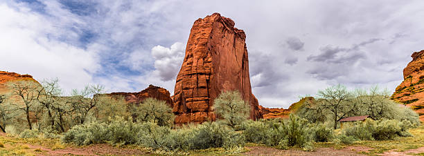 Canyon de Chelly National Monument, in northeastern Arizona, preserves nearly 5,000 years of human history within its dramatic sandstone walls. The canyon has been home to Ancestral Puebloans, known as the Anasazi, who built cliff dwellings here between 350 and 1300 CE, and to the Diné (Navajo) people who continue to live and farm within its sheltered valleys today. Carved by the forces of water and wind over millions of years, the canyon’s sheer cliffs rise to 1,000 feet above the canyon floor, revealing layers of ancient rock from the Permian period. From these rim overlooks, visitors can gaze down upon a living landscape where Navajo families maintain their traditions amidst towering formations, cottonwood groves, and sacred archaeological sites.  This scene was photographed from Canyon Road at Canyon de Chelly National Monument near Chinle, Arizona, USA.