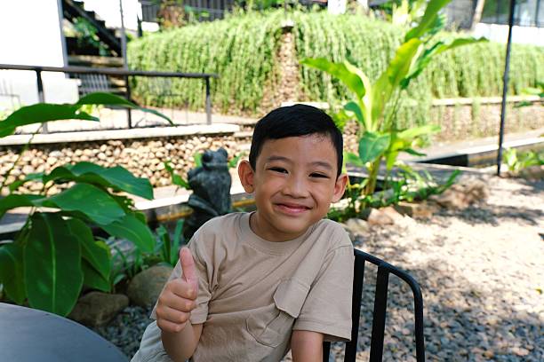 A boy sitting at a table in the park, smiling casually while enjoying the outdoor atmosphere.