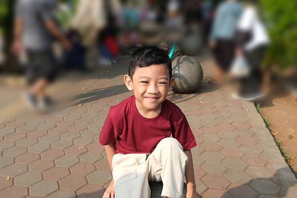 A smiling boy in a red shirt sitting casually outdoors on a sunny day. Natural portrait with candid expression and relaxed atmosphere.