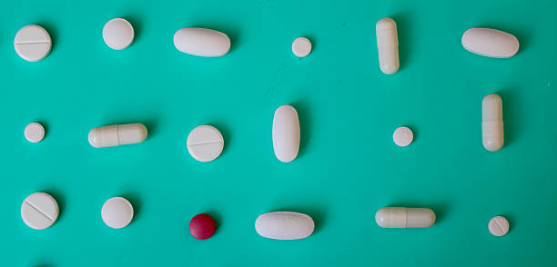 White pills, capsules, and one red pill are arranged in neat rows on a turquoise background, reminiscent of a sea wave. This minimalist and ordered shot highlights themes of health, pharmaceuticals, and scientific research.