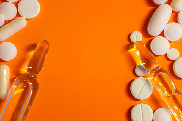 On a bright orange background, various white pills, capsules, and glass ampoules are arranged, symbolizing medicine, treatment, and health. This minimalist yet expressive composition is perfect for pharmaceutical and medical themes.