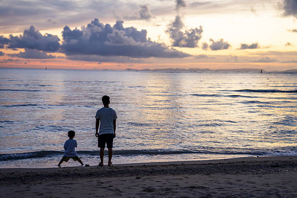 Father and son looking out over the ocean at sunset with cloudy skies