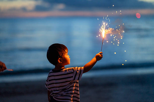 Young Asian boy holding a firework at dusk on a beach in Okinawa