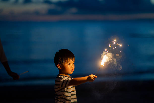Boy holds a brightly lit sparkler, illuminating the night with a magical glow.