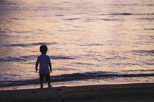 Silhouette of a girl running on water against the background of an evening sunset. Water splashes in all directions. Carefree baby fun. Happy healthy childhood.