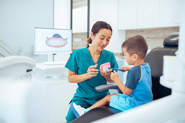 istock Female asian dentist explaining to a small boy about brushing teeth. 2231400086