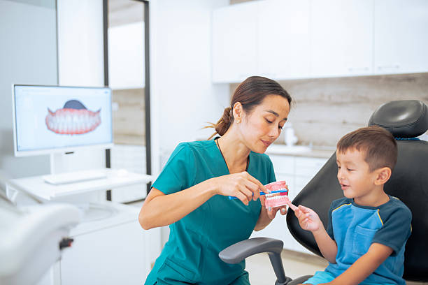 istock Female asian dentist explaining to a small boy about brushing teeth. 2231400099