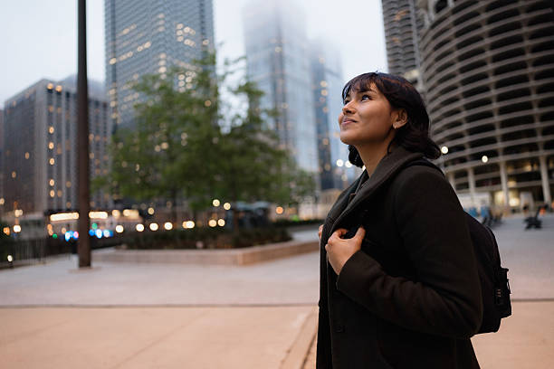 Young Latin American businesswoman gazing up at the towering skyscrapers of downtown Chicago during the enchanting dusk hours