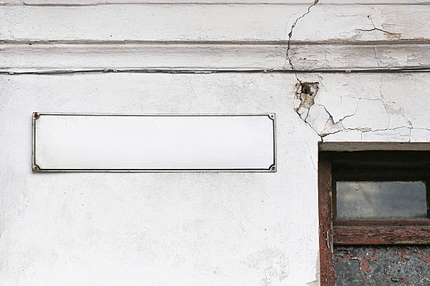 istock Old damaged building wall with cracked plaster and empty signboard above window. Weathered facade with peeling paint and broken surface texture. 2231410289