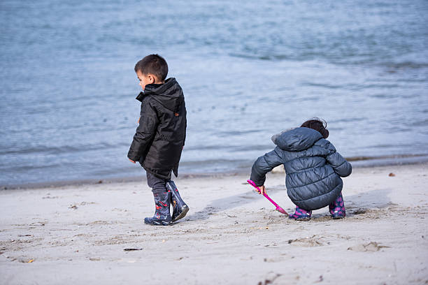 A three year old Eurasian girl plays at the beach with her boy cousin of the same age while on a winter vacation with their families at the Oregon Coast.